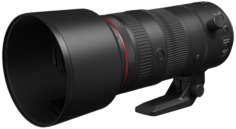 A large, black telephoto camera lens with a red ring near the front, mounted on a small, detachable tripod foot. It features control dials and switches on the side for adjustments. The lens hood is attached.