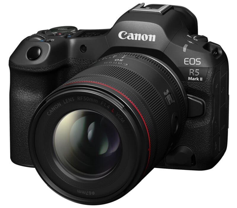 A Canon EOS R5 Mark II camera with a lens attached, featuring a sleek black body and textured grip. The lens has red and white markings, indicating specifications, and is prominently focused in the foreground.