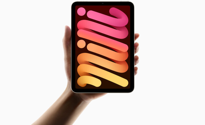 A hand holding a tablet with a colorful gradient screen displaying the word "mini" in bold letters. The background is plain white.