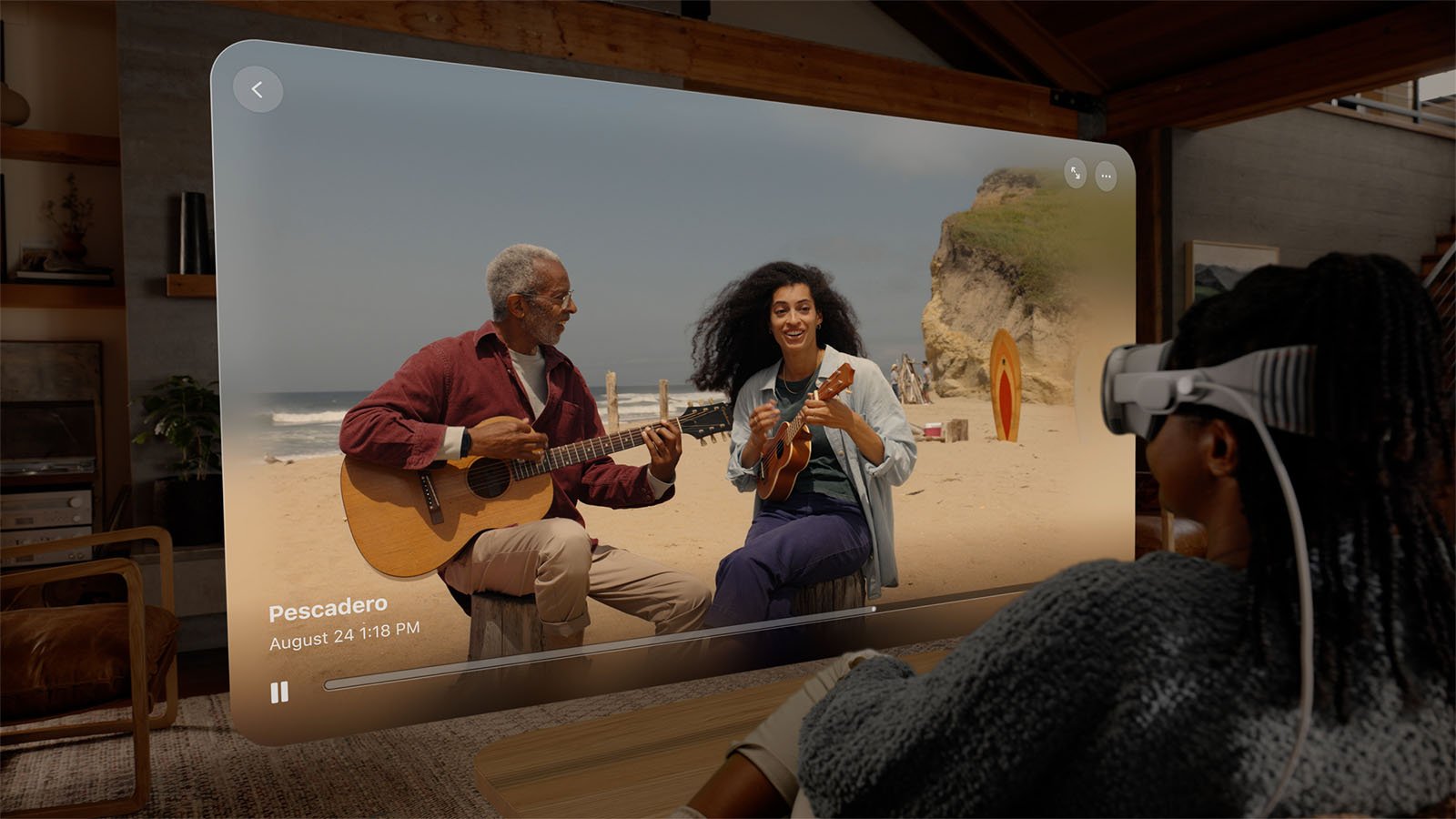 Person wearing virtual reality headset watches a scene of two people playing guitar and ukulele on a beach. There are cliffs and surfboards in the background.