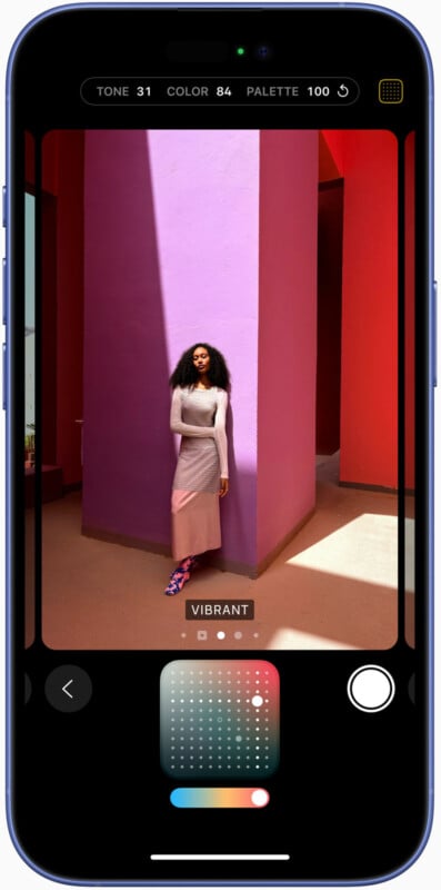 Smartphone screen displaying a photo editing app. The image being edited shows a woman leaning against a vibrant pink wall, with orange and red walls surrounding her. She is wearing a long white dress, and sunlight casts shadows on the floor.