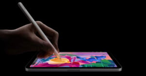 A person uses a stylus to draw colorful flowers on a tablet against a black background.