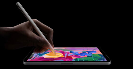 A person uses a stylus to draw colorful flowers on a tablet against a black background.