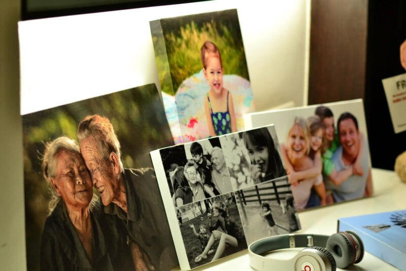 A collection of photos displayed on a lit surface. The images feature various people smiling, including an elderly couple, children playing, and a group of friends. In the foreground, a pair of headphones is visible.