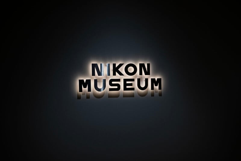 The image shows a dark background with the text "NIKON MUSEUM" in bold, capital letters. The letters have a glowing effect, casting soft shadows on the background.