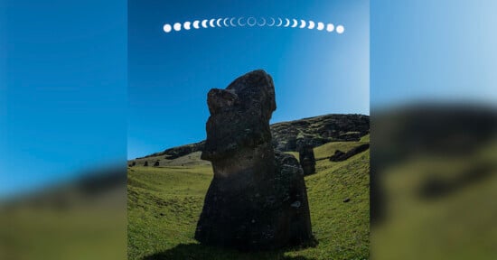 A large stone statue stands on a grassy hill under a clear blue sky. Above the statue, a sequence of moon phases is displayed in a curved line from left to right.