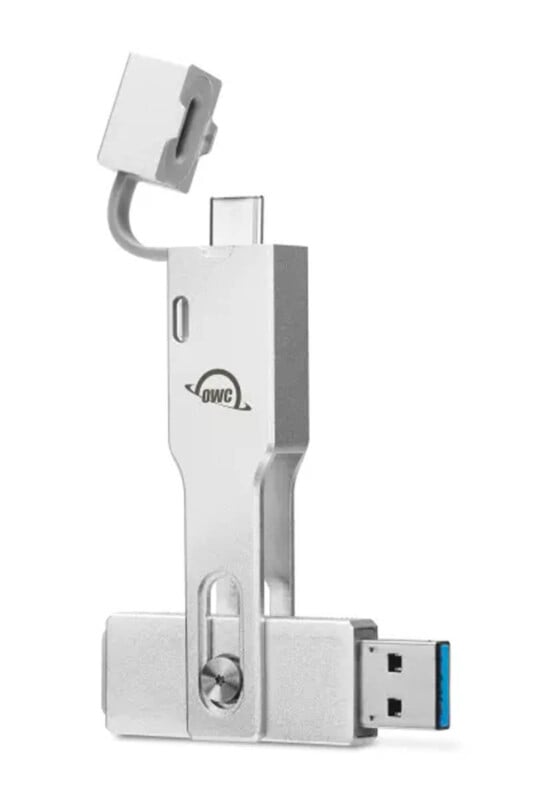 A silver multifunctional USB device with USB-A, USB-C, and Lightning connectors. The design includes a rotating mechanism, and it features the OWC logo on its side.