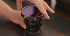 A person adjusts a circular filter on a camera lens. The scene captures a close-up of the hands gently handling the filter on a 50mm lens, with a blurred background.