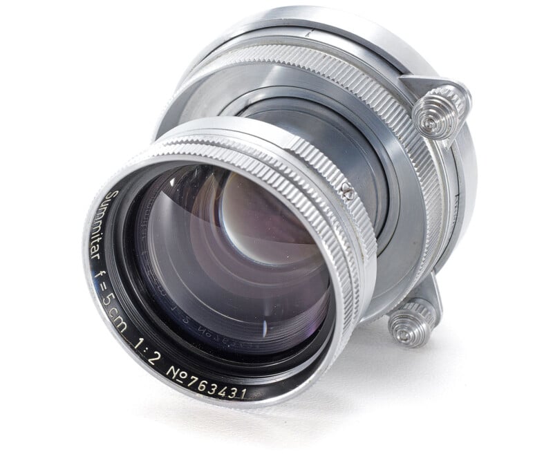 A vintage silver camera lens with engraved text showing "Summitar f=5 cm 1:2 N9763431." The lens features precision craftsmanship, with a prominent glass element and metal rings, set against a white background.