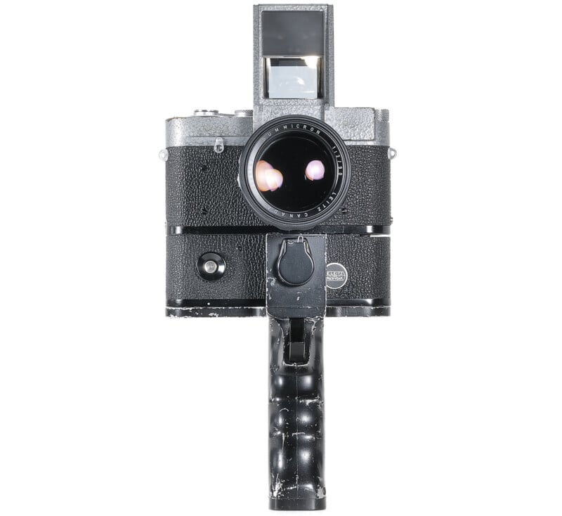 A vintage black and silver trigger grip movie camera with a large lens and a viewfinder on top, isolated on a white background.