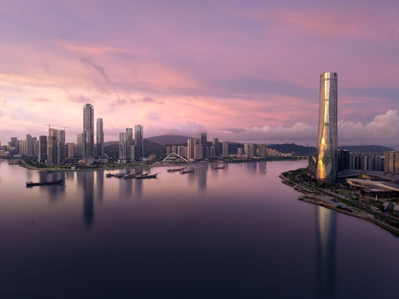 A serene cityscape at sunset with tall skyscrapers reflecting on a calm body of water. The sky is painted in pastel hues of pink and purple, and the scene is tranquil with no visible people or traffic.