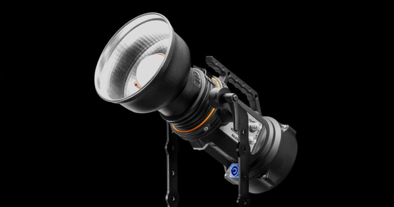 A professional studio light with a large reflector and adjustable mounts, set against a black background. The design is sleek, featuring metallic elements and a visible bulb.