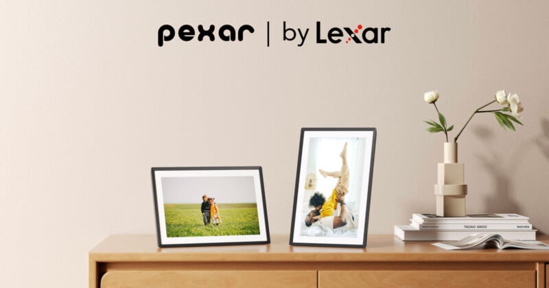 A wooden table with two framed photos: one of a couple in a field and another of a person doing a headstand. A stack of books with a simple beige vase holding two white flowers is nearby. Logos of "pexar" and "by Lexar" are on the wall.