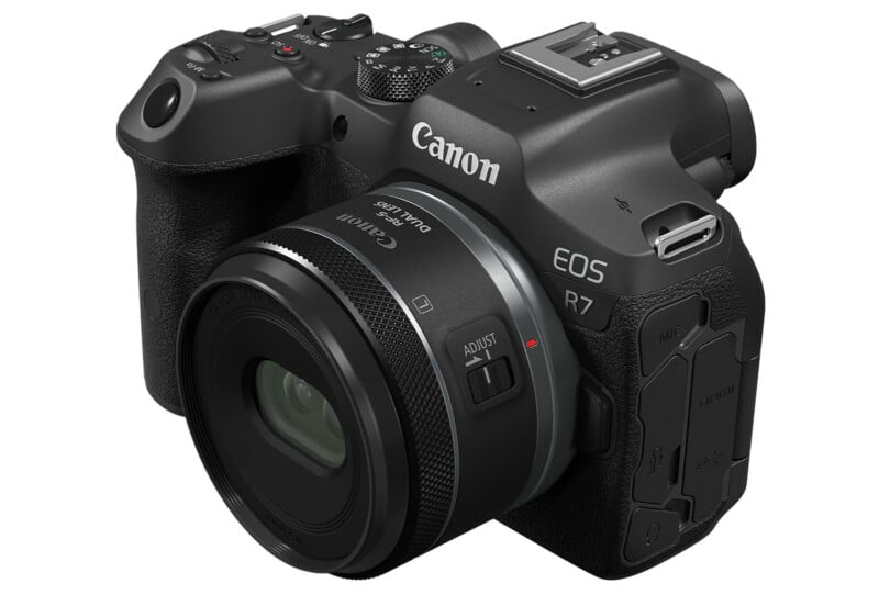 A Canon EOS R7 digital camera with a lens attached is shown. The camera features various buttons and dials for settings adjustments. It is angled slightly, revealing the brand name and model prominently on the body.