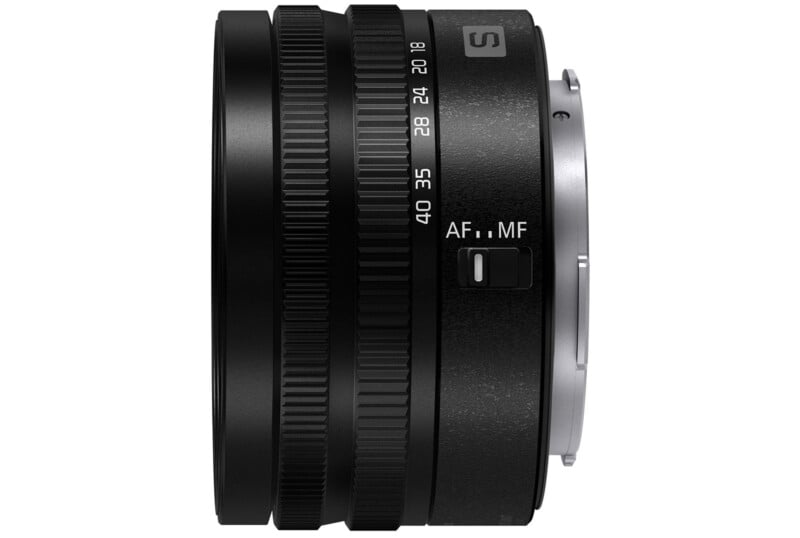 A close-up view of a camera lens with various settings visible, including a focus mode switch labeled "AF/MF." The lens has a textured grip and numerical markings around the edge. It features a metallic mount on one end.