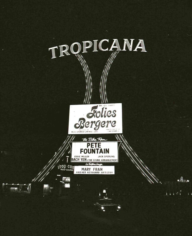 A vintage black and white photo of the Tropicana sign in Las Vegas at night, featuring advertisements for "Folies Bergere" and performances by Pete Fountain and Mary Kaye Trio. The sign is illuminated, highlighting the names and events.