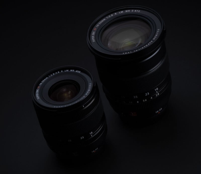 A close-up of two camera lenses placed on a dark surface. The lens on the left is smaller and wider, while the lens on the right is larger with a longer focal length. The lenses have markings and numbers indicating their specifications.