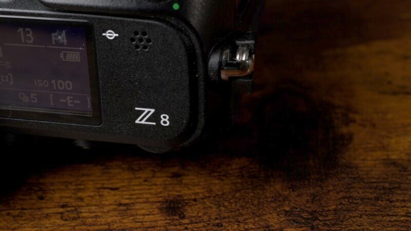 Close-up of a black camera body with "Z 8" printed on it, partially showing a screen with camera settings. The surface under the camera is a textured wooden surface.