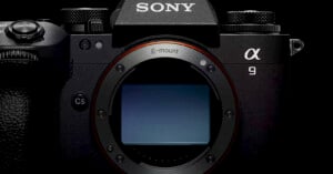 Close-up view of a Sony Alpha 9 camera body, showcasing the E-mount connection in the center. The camera is black, with textured grips and visible branding at the top. The camera is displayed against a dark background.