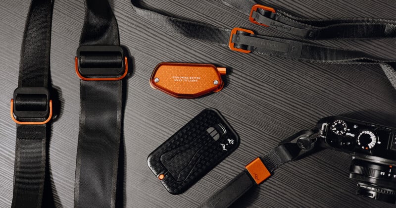 Photography accessories laid out on a dark surface, including camera straps with orange accents, a black camera, and a small orange device. The arrangement showcases a modern, sleek design.