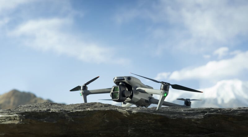 A drone hovers just above a rocky surface with a scenic backdrop of mountains and a partly cloudy sky.