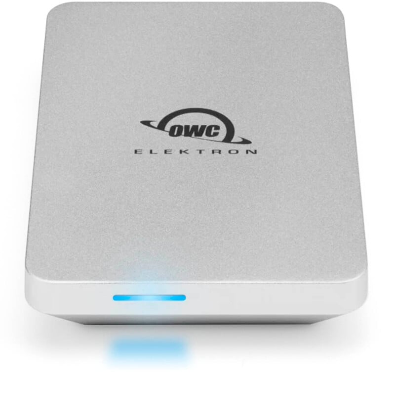 A silver external hard drive with rounded edges, featuring the logo "OWC ELEKTRON" on top. A small blue LED light is illuminated on the front, indicating power or activity.