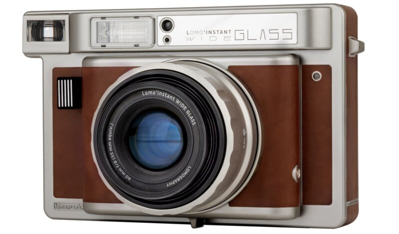 A retro-style instant camera with a brown and silver body. The camera features a large lens and a prominent viewfinder. The label reads "Lomo'Instant Wide Glass.