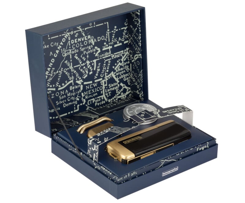 An elegant, open gift box featuring a black and gold harmonica. The box interior is adorned with a map design and includes a cleaning cloth and a small storage compartment.