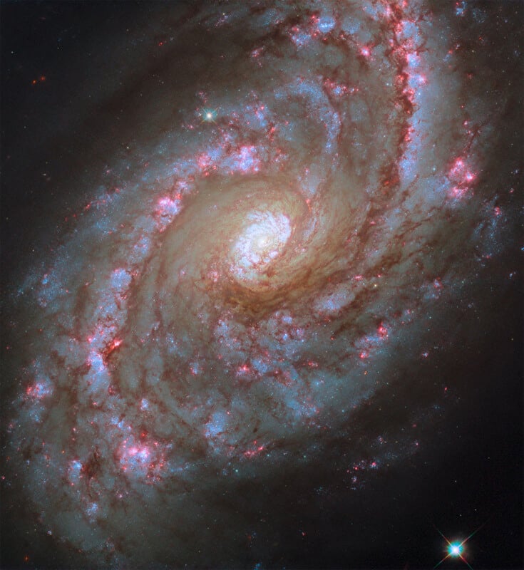 Image of a spiral galaxy with a bright core surrounded by swirling arms of stars, dust, and gas. The arms display vibrant colors such as blue and pink against a dark space background.