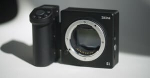 A black Sitina S1 camera body without a lens is placed on a light surface. The camera body features a sensor mount and a side grip with control buttons.