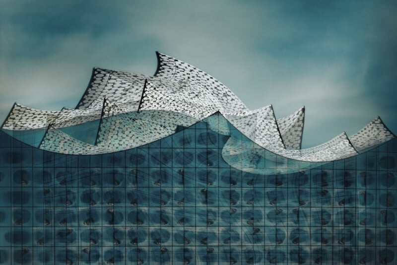 An architectural structure with a modern, wave-like rooftop design against a cloudy sky. The building's facade features a glass exterior with a grid pattern, creating a reflective and textured appearance. The overall look is futuristic and innovative.