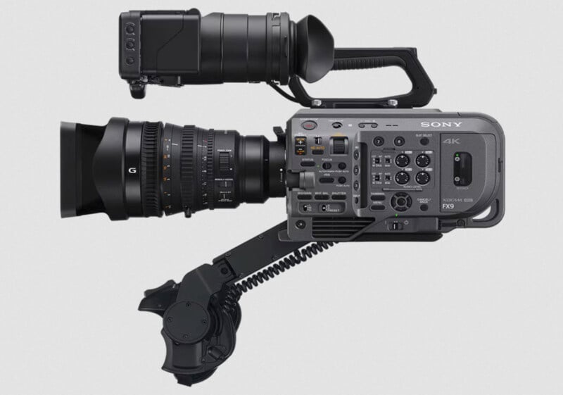 Side view of a Sony FX9 4K professional video camera with various buttons and controls visible. The camera is equipped with a large zoom lens and an adjustable grip handle.