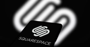 A smartphone screen displaying the Squarespace logo is in focus, with a blurred, larger version of the same logo in the background. The logos consist of interlocking, abstract shapes, representing the branding of the website-building platform.