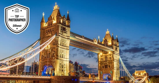 A beautifully illuminated Tower Bridge at dusk, with a "Top Photographer Winner" badge displayed in the top left corner. The bridge's lights shine against a backdrop of a darkening sky and city skyline.