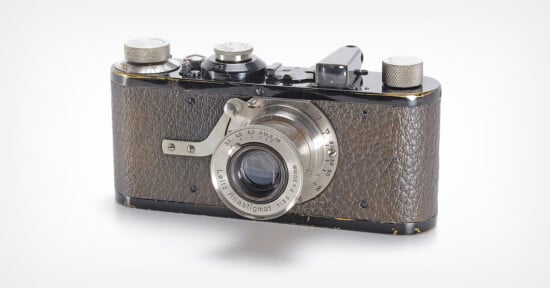 A vintage, black and silver camera with a textured, brown body and a large lens. It features two metallic dials on top and a streamlined design with visible wear.