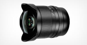 A wide-angle camera lens with a sleek, black design featuring a smooth barrel and visible focus and zoom rings. The glass element at the front is large and curved, reflecting light. The background is white.