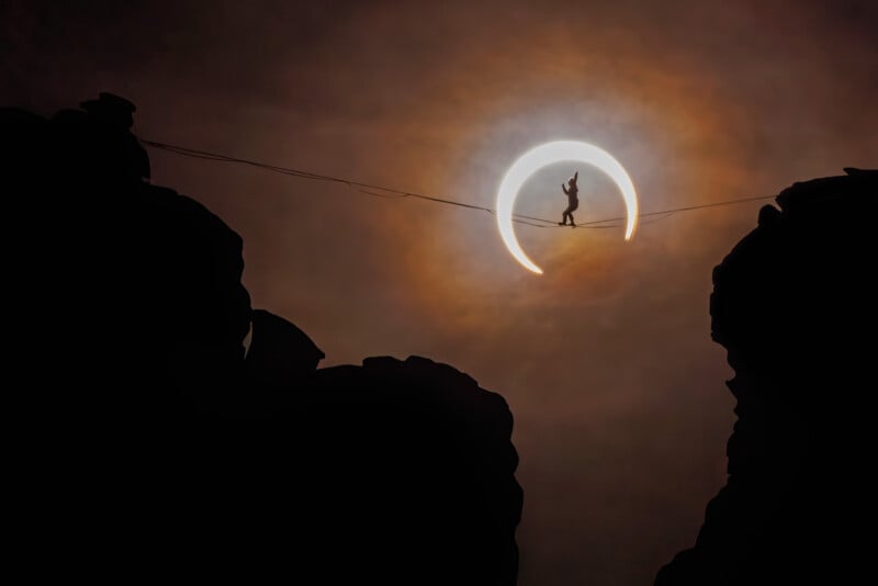 A silhouette of a person walking on a tightrope between two rocky cliffs, with a glowing, partially eclipsed sun creating a dramatic halo effect behind them in the sky.