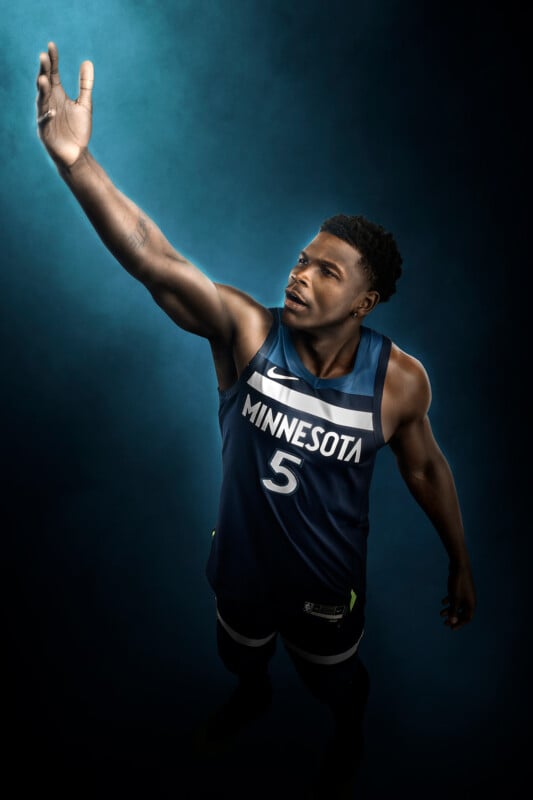 A basketball player in a Minnesota jersey, number 5, is captured mid-jump against a blue background, reaching up with one arm.