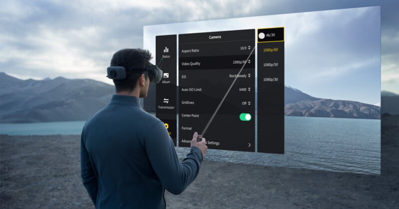 A person wearing a virtual reality headset stands outdoors near a lake and mountains, interacting with a large augmented reality interface displaying camera settings and options.