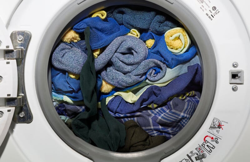 Vue d'un tambour de machine à laver rempli de serviettes et de vêtements de différentes couleurs, notamment des motifs bleus, jaunes, verts et à carreaux.