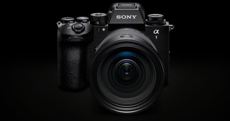 Front view of a black Sony Alpha digital camera with a large lens, set against a dark background. The camera's model is prominently displayed.