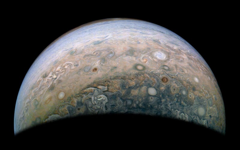 A striking image of Jupiter's northern hemisphere, showcasing its swirling clouds and intense storm systems in hues of blue, brown, and white. The planet's vast, dynamic atmosphere is depicted against the blackness of space.