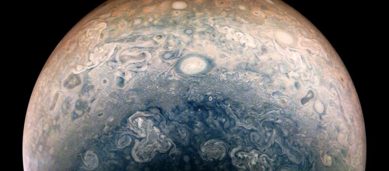 A detailed view of Jupiter's swirling cloud patterns, showcasing various shades of blues, whites, and grays. The image highlights the planet's turbulent atmosphere with several circular and spiral formations.