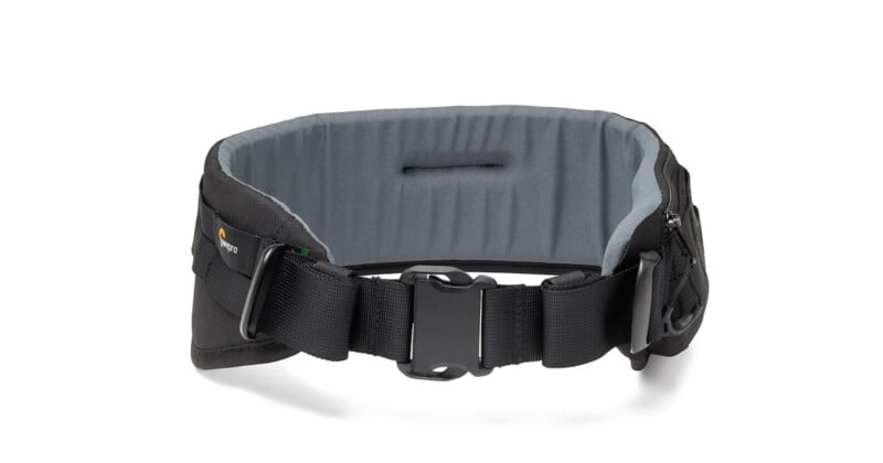 A black camera belt with padding, featuring a secure buckle in the center. The belt has loops on the sides for holding accessories, and a small logo is visible on the left. The interior is lined with gray cushioning for comfort.