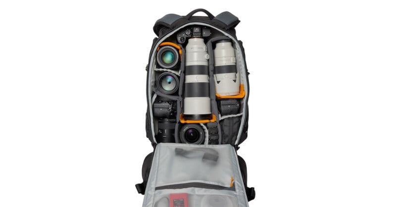 An open camera backpack displaying various photography equipment, including multiple camera lenses neatly organized in padded compartments. The backpack has a partially open flap with additional pockets and visible camera accessories.