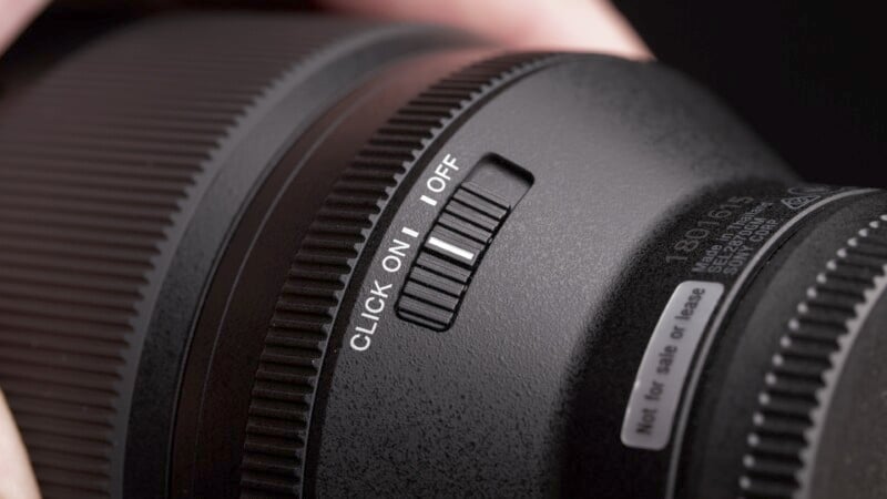 Close-up of a camera lens with a focus on a switch labeled "CLICK ON/OFF." The lens has textured and smooth surfaces, and a label indicating "not for sale or lease" is partially visible.