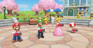 Four animated characters, including two with red and green hats, a princess, and a character with a red-spotted mushroom hat, stand in a sunny town square holding red cameras. Cherry blossom trees and a building are in the background.