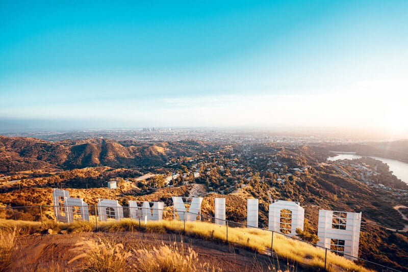 Une vue derrière le célèbre panneau Hollywood, surplombant les collines et le vaste paysage urbain de Los Angeles sous un ciel bleu clair.