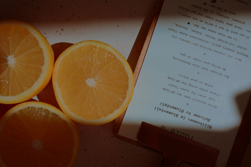 Sliced oranges are placed next to a clipboard with a menu titled "Table 3," partially visible in dim lighting. The image has a warm, moody atmosphere.