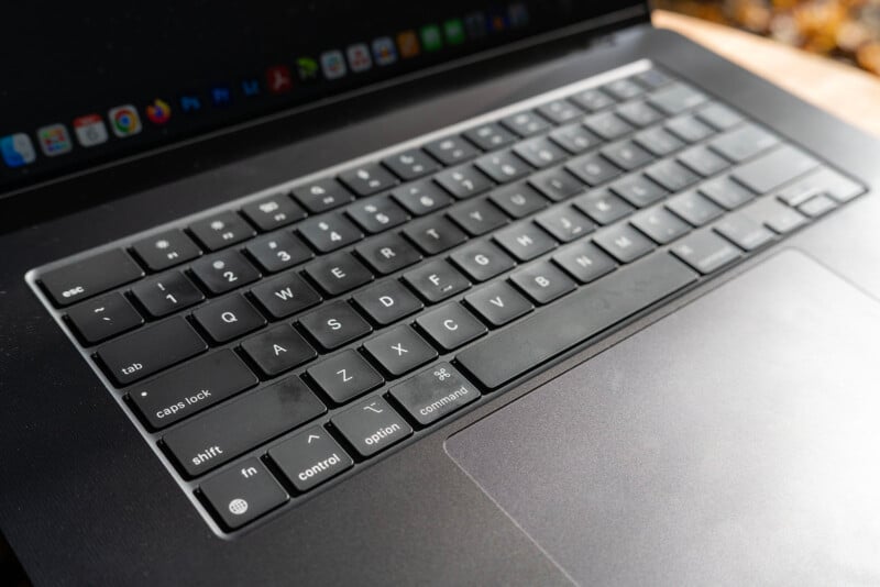 A close-up view of a black laptop keyboard, showing keys including shift, control, and command. The touchpad is visible below the keyboard, and part of the screen with app icons is seen at the top.